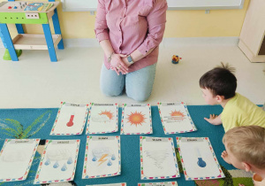 Zdjęcie opiekunki tłumaczącej dzieciom na czym polegać będą zaplanowane zajęcia.