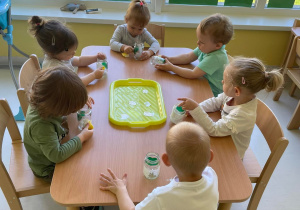 Zdjęcia dzieci z Grupy Żabki siedzących przy stoliku, podczas wykonywania prezentu na Dzień Mamy.