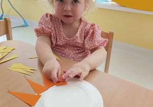 Laura pozuje do zdjęcia podczas przyklejania na swój talerzyk pomarańczowego promyczka.