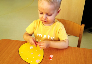 Mały chłopczyk podczas ozdbiania swojego żółtego jajka z papieru.