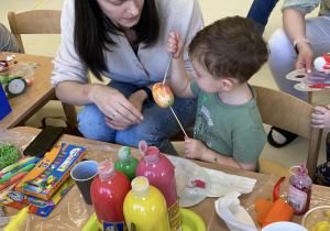 Mama Stanisława przygląda się jak chłopiec maluje pędzelkiem stropianowe jajko nabite na patyczek szaszłykowy.