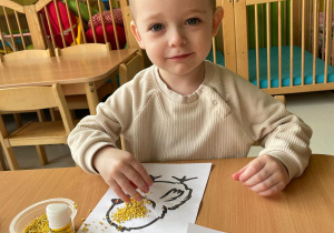 Mały chłopiec posypuje kaszą kurczaka narysowanego na kartce.