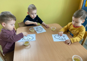 Dzieci siedzące przy stoliku podczas wykonywania swoich kurczaczków.