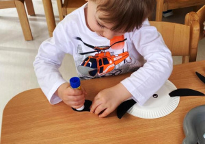 Chłopiec smaruje klejem czarną łatkę z papieru.