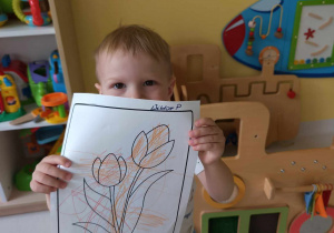 Wiktor pokazuje opiekunce robiącej zdjęcie pokolorowanego przez siebie tulipanka.