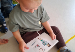 Chłopiec przygląda się ilustracji, na której jest pani doktor i przyrządy lekarskie.