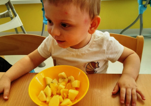 Usmiechnięty chłopiec z miseczką pełną pokrojonych owoców.