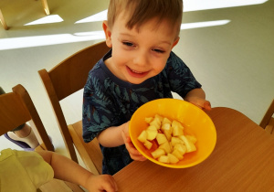 Zdjęcie chłopca unoszącego miskę ze swoją sałatką owocową do góry.