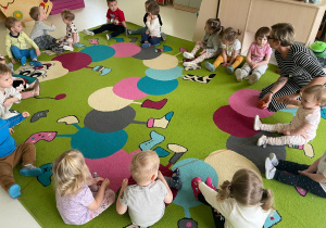 Dzieci wraz z opiekunką siedzące obok siebie tworząc koło.