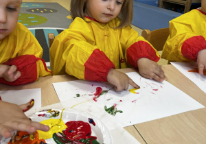 Marcelina maluje na kartce paluszkiem z żółtą farbą.
