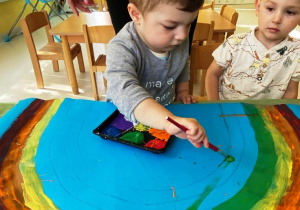 Mały chłopiec dodaje do szablonu tęczy zieloną farbę.
