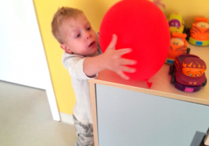 Chłopiec sięga z półki czerwony balonik.