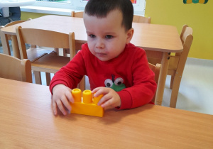 Chłopiec siedzi przy stoliku z żółtym klockiem.