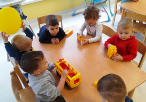 Dzieci siedzące przy stole z żółtymi zabawkami.