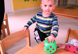 Chłopiec siada do stołu z zieloną kostką.