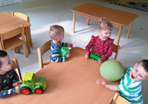 Dzieci z zielonymi zabawkami siedzą przy stole.