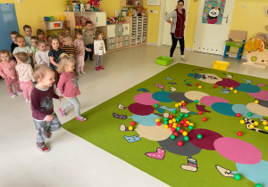 Zdjęcie dzieci przyglądających się na kolorowe piłeczki rozrzucone na dywanie.
