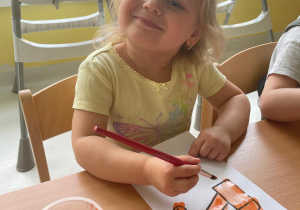 Usmiechnieta dziewczynka maluje szablon kranu pomarańczową farbą.