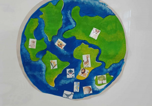 Zdjęcie Kuli Ziemskiej z przyklejonymi przez dzieci kontynentami i obrazkami zwierząt i roślin morskich oraz lądowych.