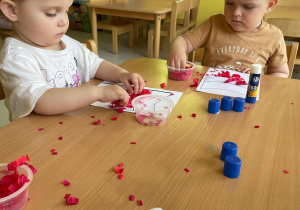 Dzieci naklejają kuleczki z czerwonej bibuły na dolną część flagi.