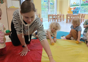 Opiekunka pokazuje dzieciom na czym polegają zaplanowane zajęcia.