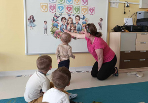 Opiekunka opisuje dzieciom zdjęcia postaci przyczepionych na tablicy.