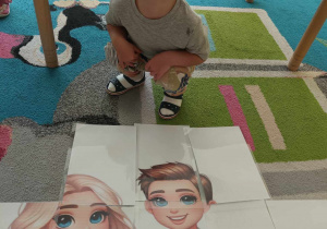 Uśmiechnięty Marcel kuca przed ułożonym obrazem z puzzli XXL.