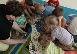 Zdjęcie dzieci i opiekunki ozdabiających wspólnie szablon sukienki mamy.