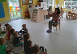 Opiekunka pokazuje dzieciom obrazek przedstawiający rodziców.