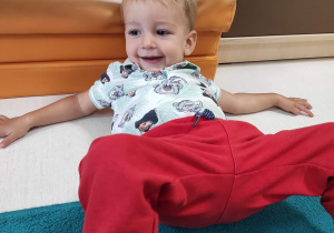 Fotografia Tymoteusza siedzącego na dywanie oraz opierającego się plecami o materac.