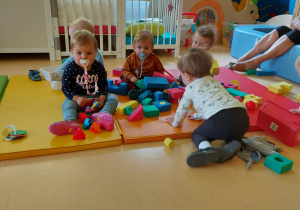 Fotografia dzieci bawiących się piankowymi klockami na materacu.