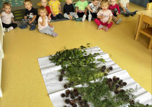 Zdjęcie dzieci z grupy Motylki przygotowujących się i siedzących przed ścieżką sensoryczną przygotowaną przez opiekunki do zajęć.