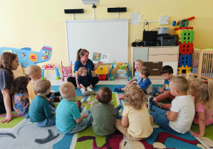 Opiekunka czyta dzieciom pierwsze strony książeczki.