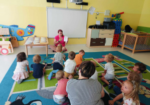 Zdjęcie dzieci i opiekunki z grupy Pszczółki siedzących na dywanie i przygotowujących się do zajęć pt. ,,SZYKUJEMY FORMĘ NA WAKACJE''.