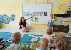 Opiekunka pokazuje oraz opisuje dzieciom miejsca, w które można jechać na wakacje i co można na nich robić.