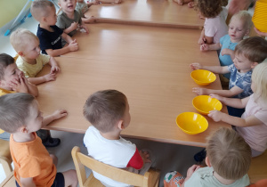 Dzieci siedzące wokół stołu i czekające na zajęcia kulinarne.