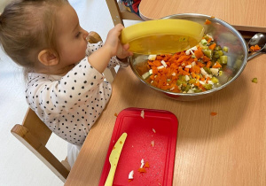 Fotografia dziewczynki wsypującej pokrojone warzywa do miski.