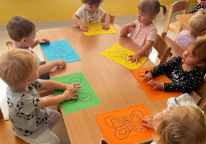 Zdjęcie dzieci siedzących przy stoliczku, przygotowujących się do dekorowania swoich motylki kropeczkami.