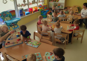 Zdjęcie dzieci z grupy Pszczółki siedzących przy stolikach, które układają drewniane układanki.