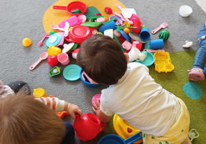 Dzieci bawiące się na dywanie plastikowymi kuchennymi akcesoriami.