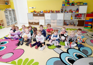 Zdjęcie dzieci z grupy Biedroneczki siedzących na dywanie ze swoimi pluszowymi misiami.