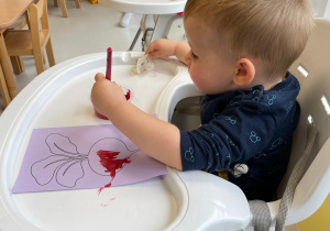 Mały chłopiec siedzący w foteliku malują farbą szablon buraka.