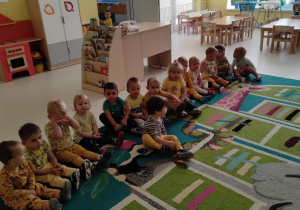 Pamiątkowe zdjęcie dzieci z grupy Pszczółki, siedzących na dywanie w żółtych ubraniach z okazji Dnia Koloru Żółtego.