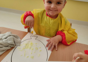 Fotografia Arturka malującego swojego papierowego balonika za pomocą wacikowych patyczków z żółtą farbą.