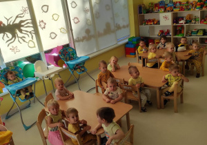 Dzieci z grupy Pszczółki siedzące w żółtych ubraniach przy stoliczkach z okazji Dnia Koloru Żółtego.