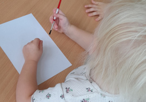 Dziewczynka trzymająca w dłoni pędzelek w czasie zajęć.