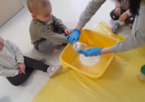 Dziecko wraz z opiekunką przesypuje mąkę do miski.
