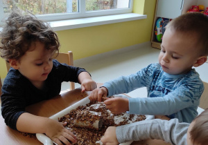 Bruno i Filipek wspólnie posypują papierową rolkę liśćmi.